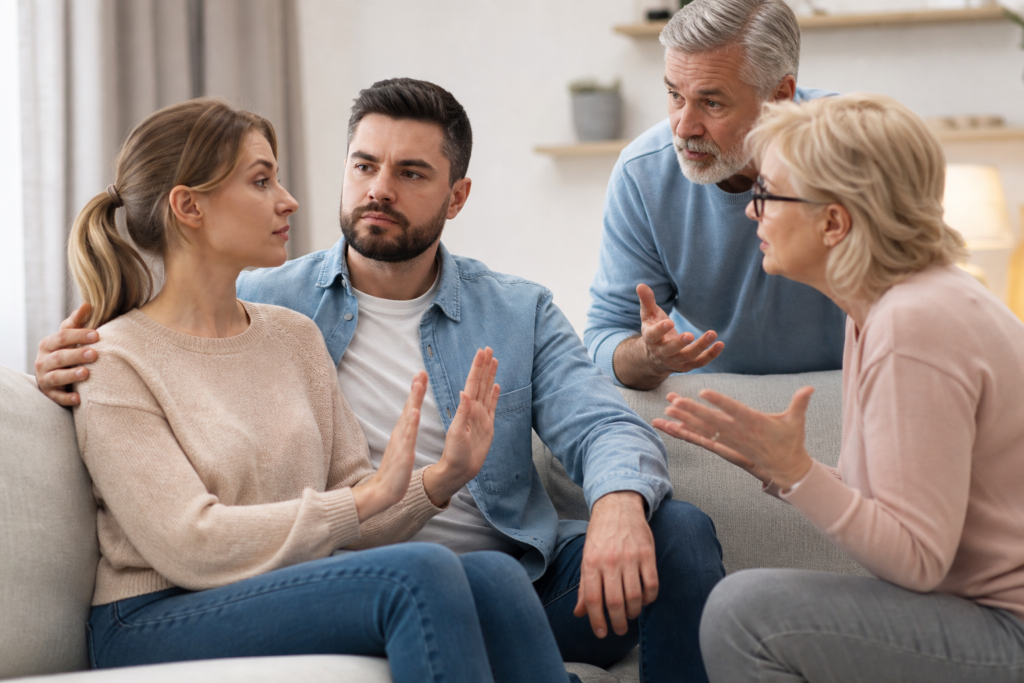 a distressed couple on a couch with parents, one gesturing stop, representing setting boundaries with in-laws.