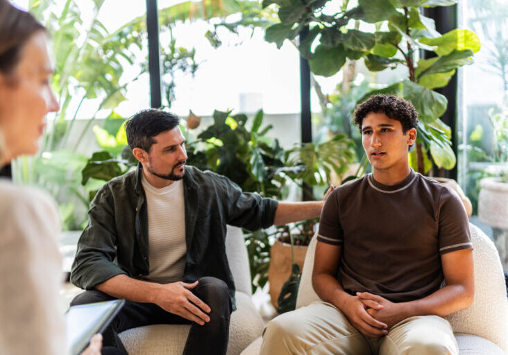 Father and son talking to psychotherapist during psychotherapy session