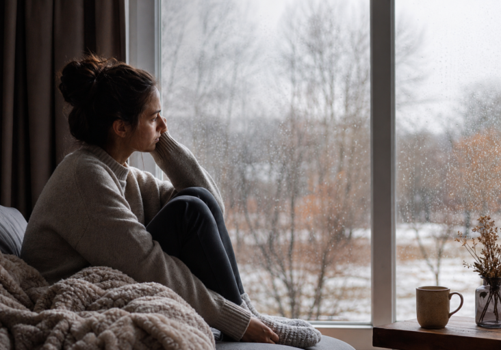woman looking out a rainy window, experiencing seasonal depression anxiety during winter.